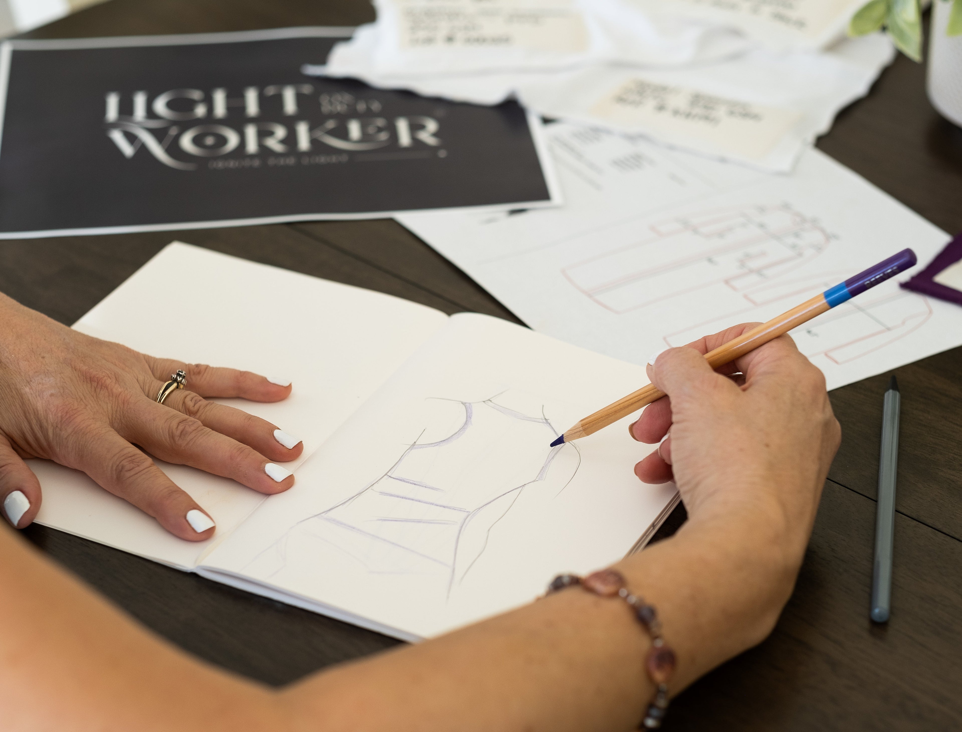 Person drawing on a piece of paper with a pencil, surrounded by business cards and a plant.